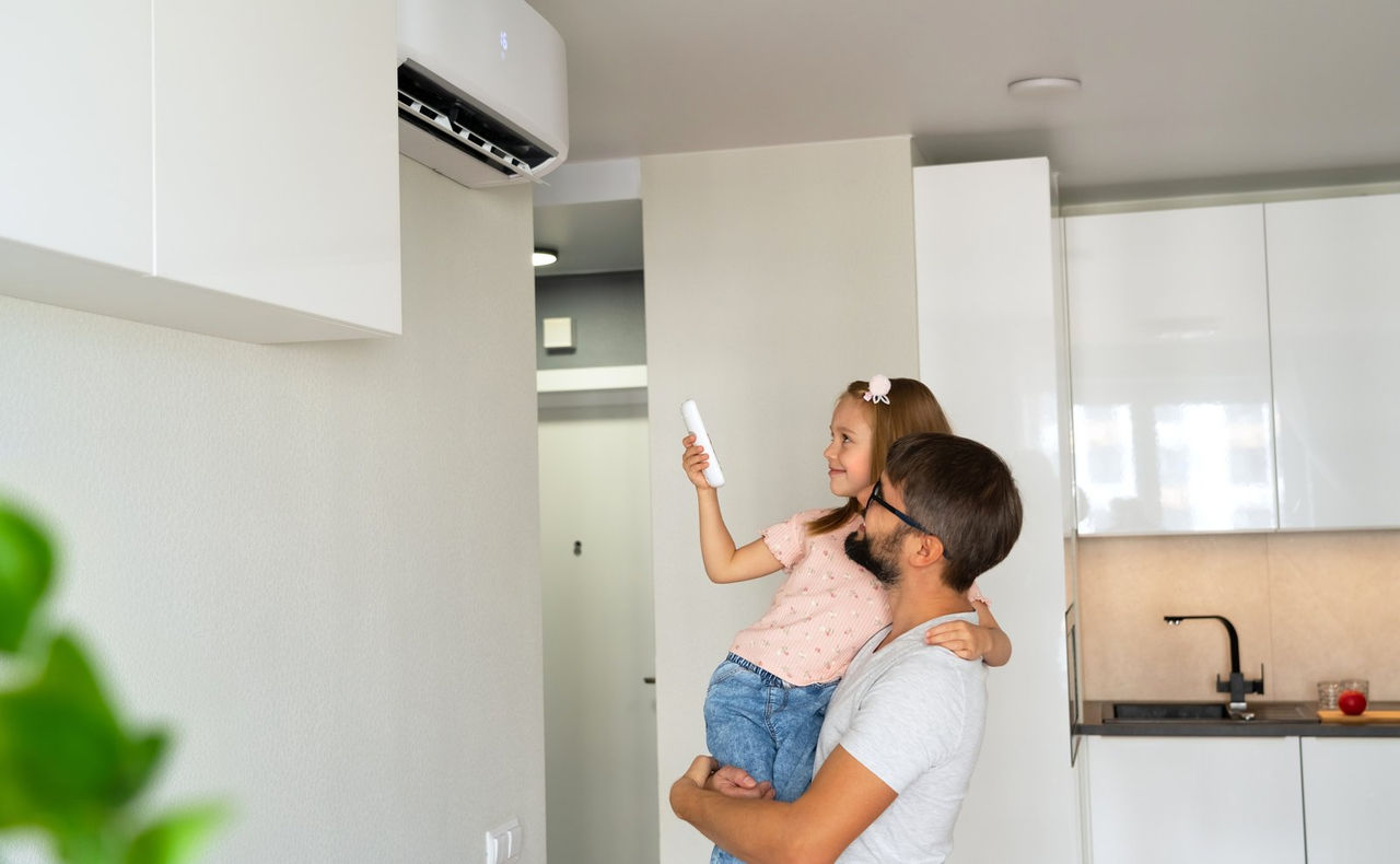 Father holding his daughter as she points a remote at a wall-mounted air conditioner at home